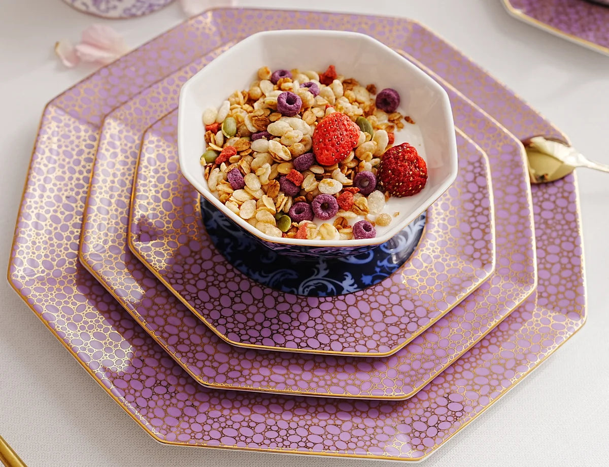 Blooming Baroque’un mor, altın renkli desenli tabakları üzerinde meyveli granola kasesi.